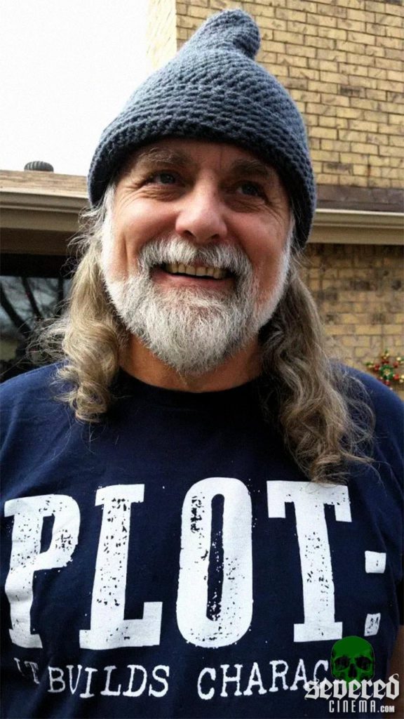 Smiling Bret McCromick wearing a navy blue t-shirt with the word "Plot"