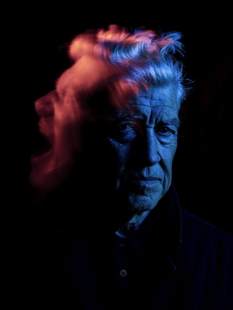 Portrait photo of David Lynch with lighting hues of blue and red.