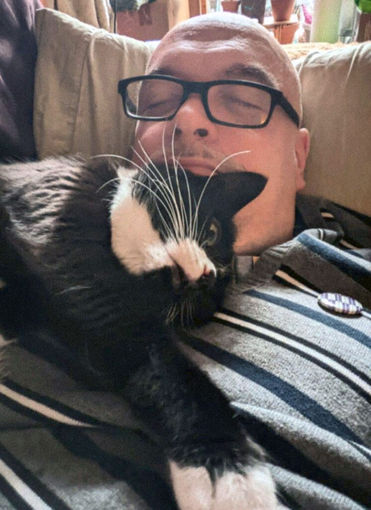 Robin Bougle laying on a couch with his black cat